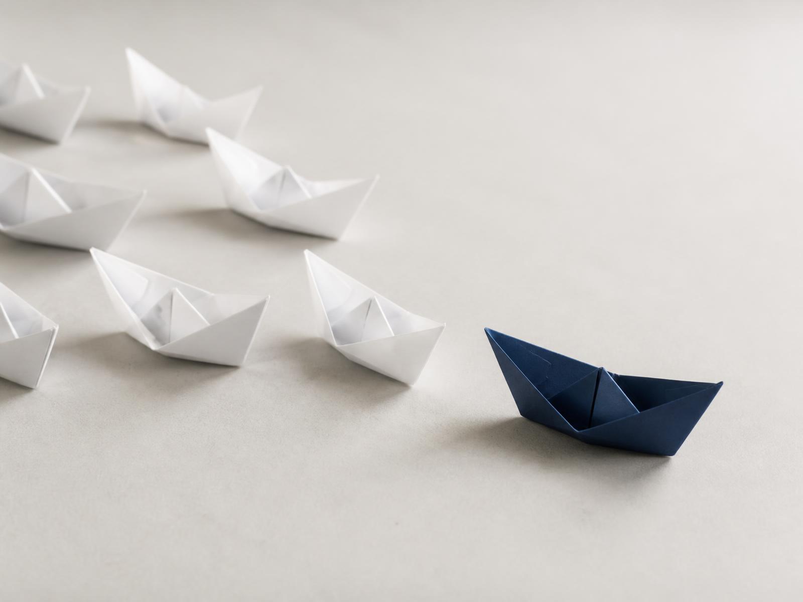 White paper boats following a single deep navy paper boat
